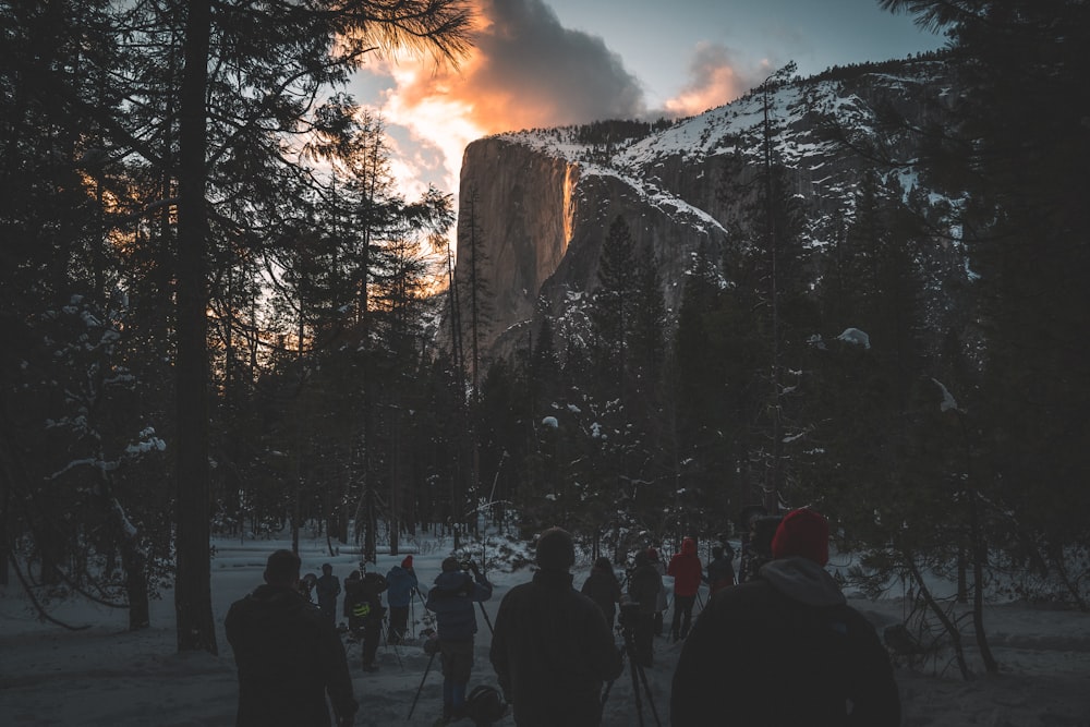 crowd on open field surrounded by trees near mountain