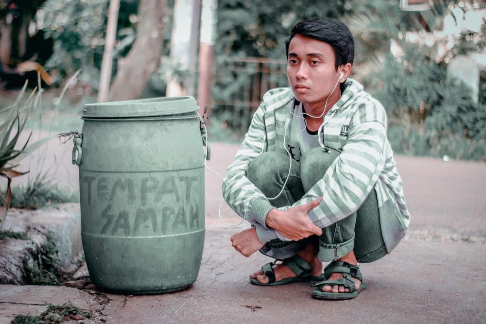 man sitting beside trash bin during daytime