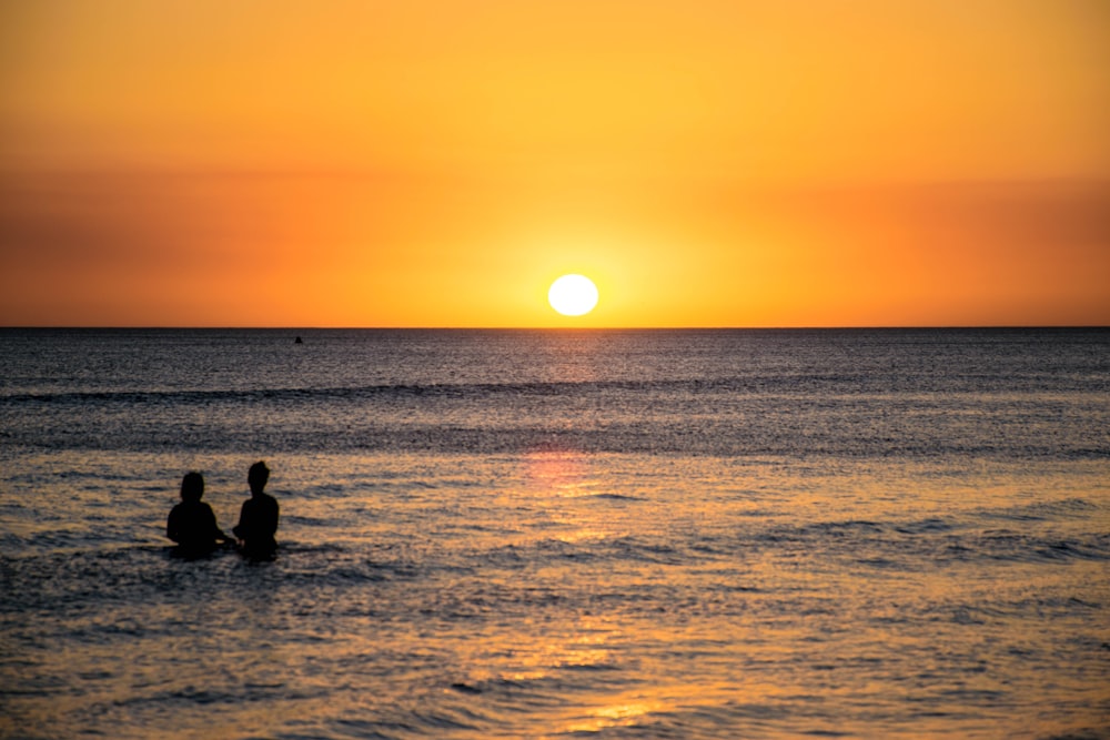silhouette photography of two persons sitting beside body of water
