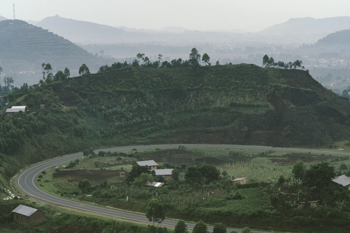 A road winding through green hills and farmland in Uganda