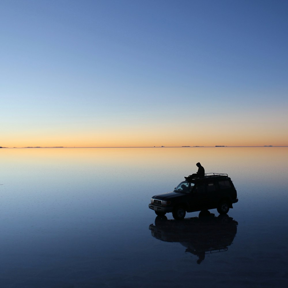 photographie de silhouette d’une personne assise sur le toit de la voiture