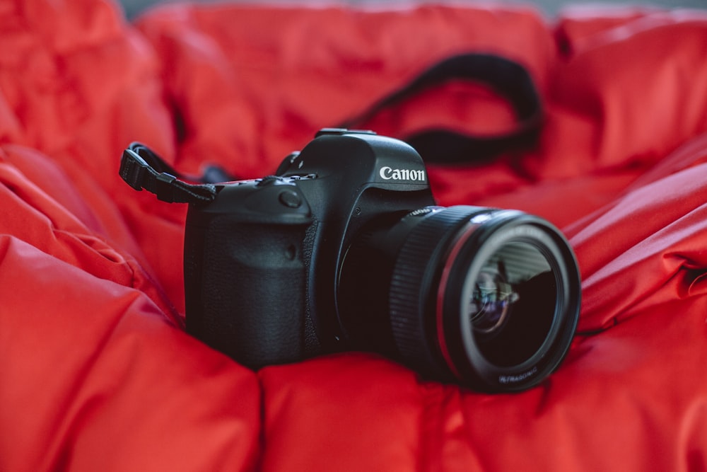 fotografia de foco seletivo da câmera Canon DSLR preta em tecido vermelho