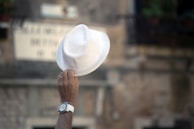 Hands adjusting a Lumina Apparel hat, with a blurred cityscape in the background.