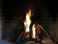 Burning logs with bright flames in a brick fireplace, casting a warm and cozy atmosphere.