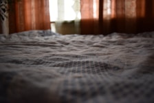 Close-up of a dorm bed with soft linens and a privacy curtain slightly pulled back.