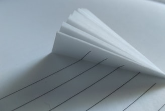 Several stacked sheets of lined paper create a shadowed effect, with the black lines providing contrast against the white background.