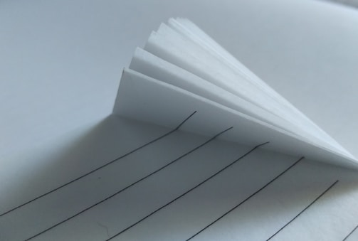 Several stacked sheets of lined paper create a shadowed effect, with the black lines providing contrast against the white background.