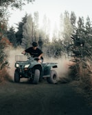 A group of riders on blue ATVs kicking up dust on a forest trail under a bright sky.