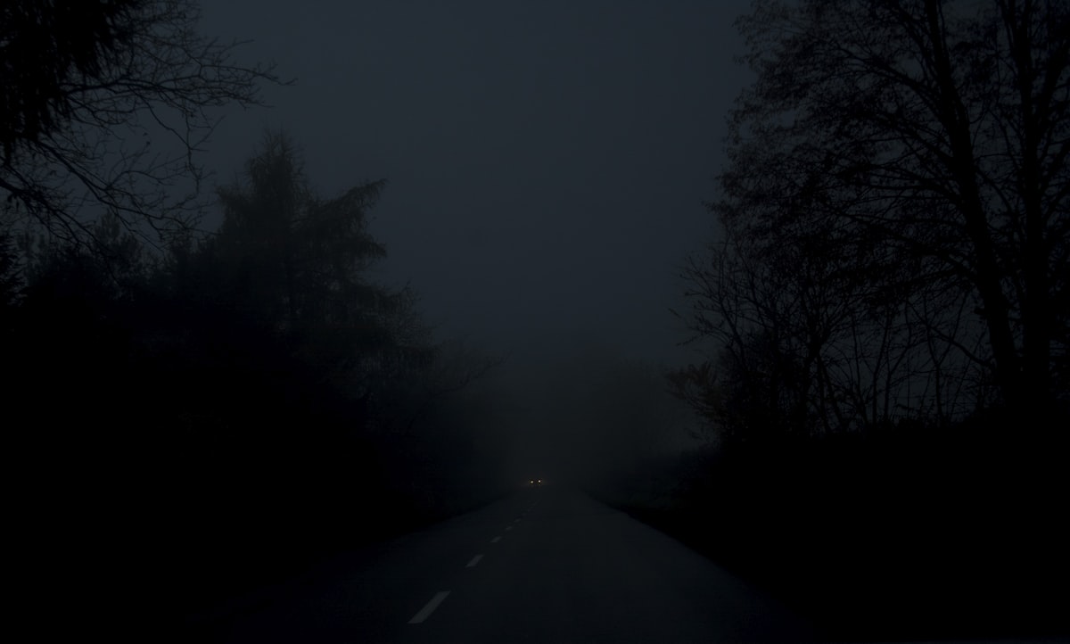 A solitary figure on a long empty road stretching toward distant mountains at dusk