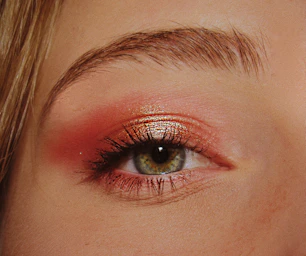 Primer plano del ojo de una mujer con maquillaje de sombras de ojos rosas y doradas