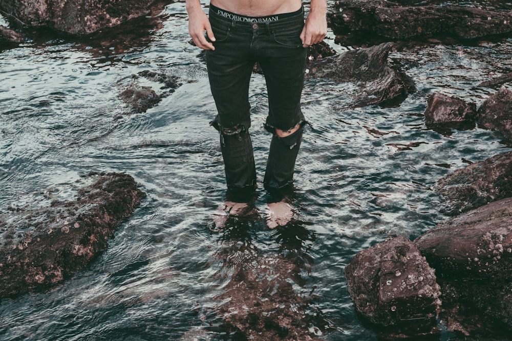 man wearing black distressed jeans while standing on stream water