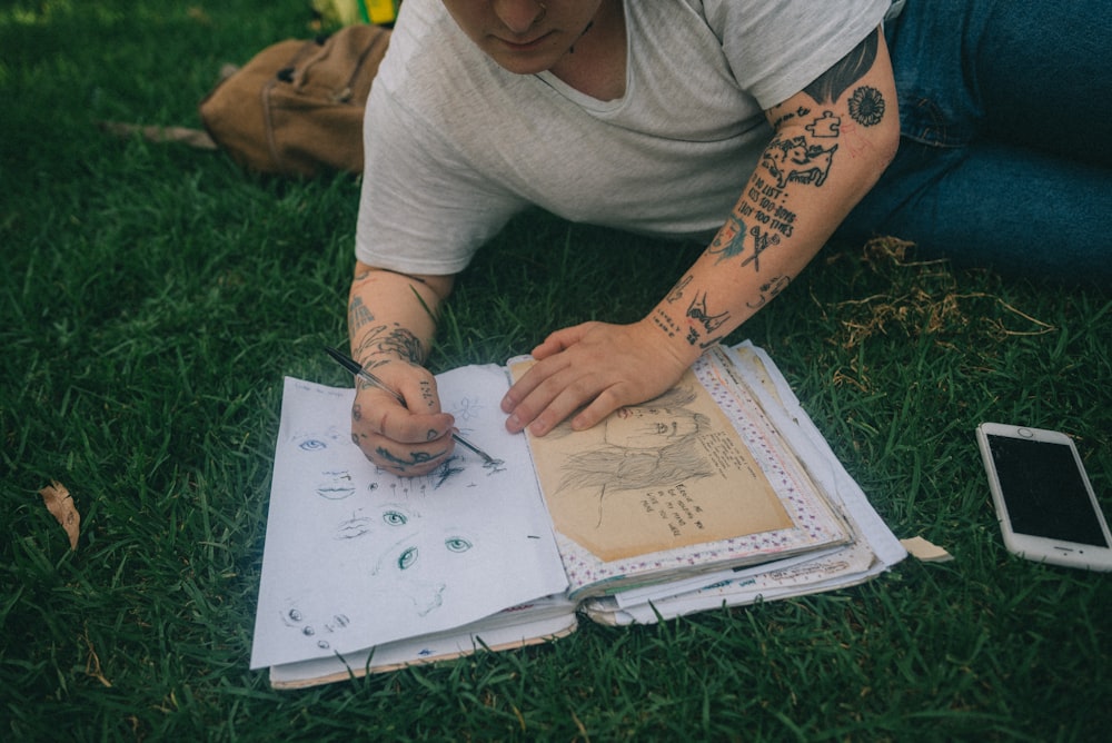 man wearing grey shirt lying on grass drawing