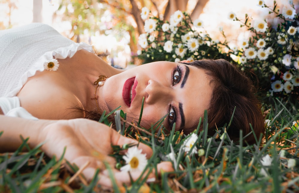 woman wearing white lying on grass near white flowers