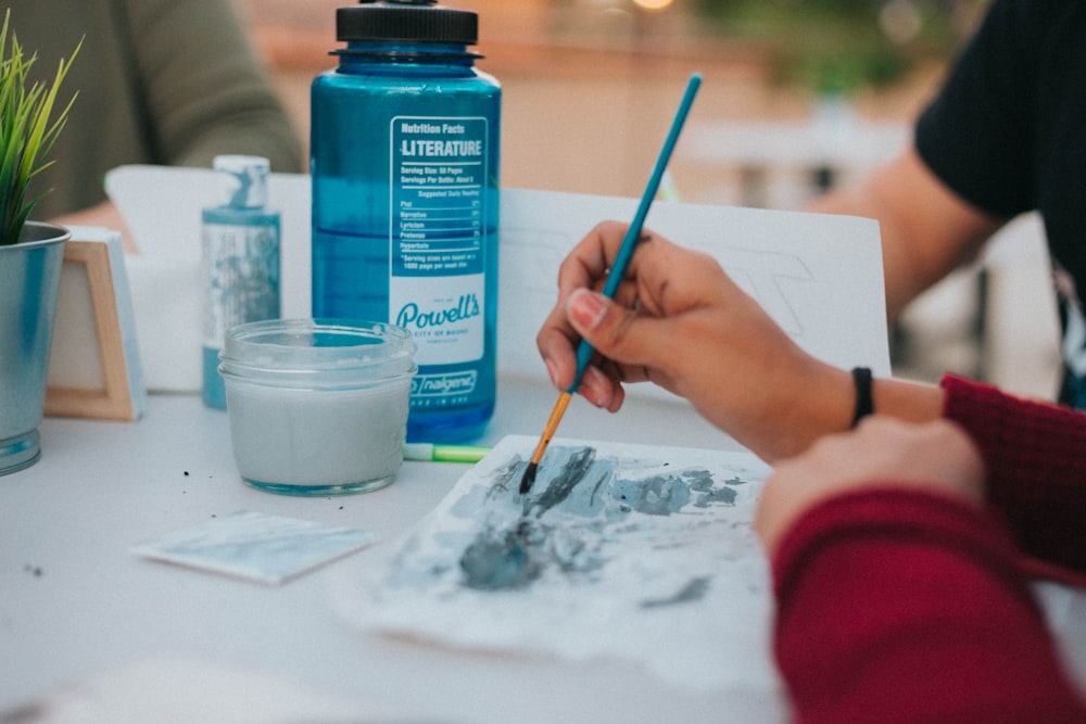 pessoa segurando pintura de pincel azul no papel na mesa