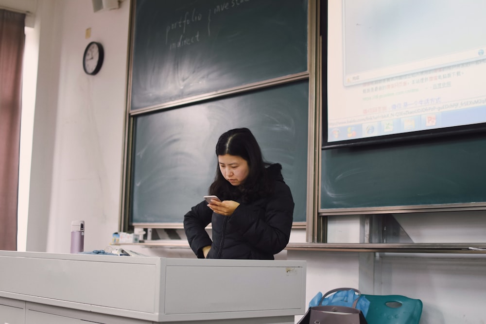 woman wearing black hoodie using smartphone near chalk board