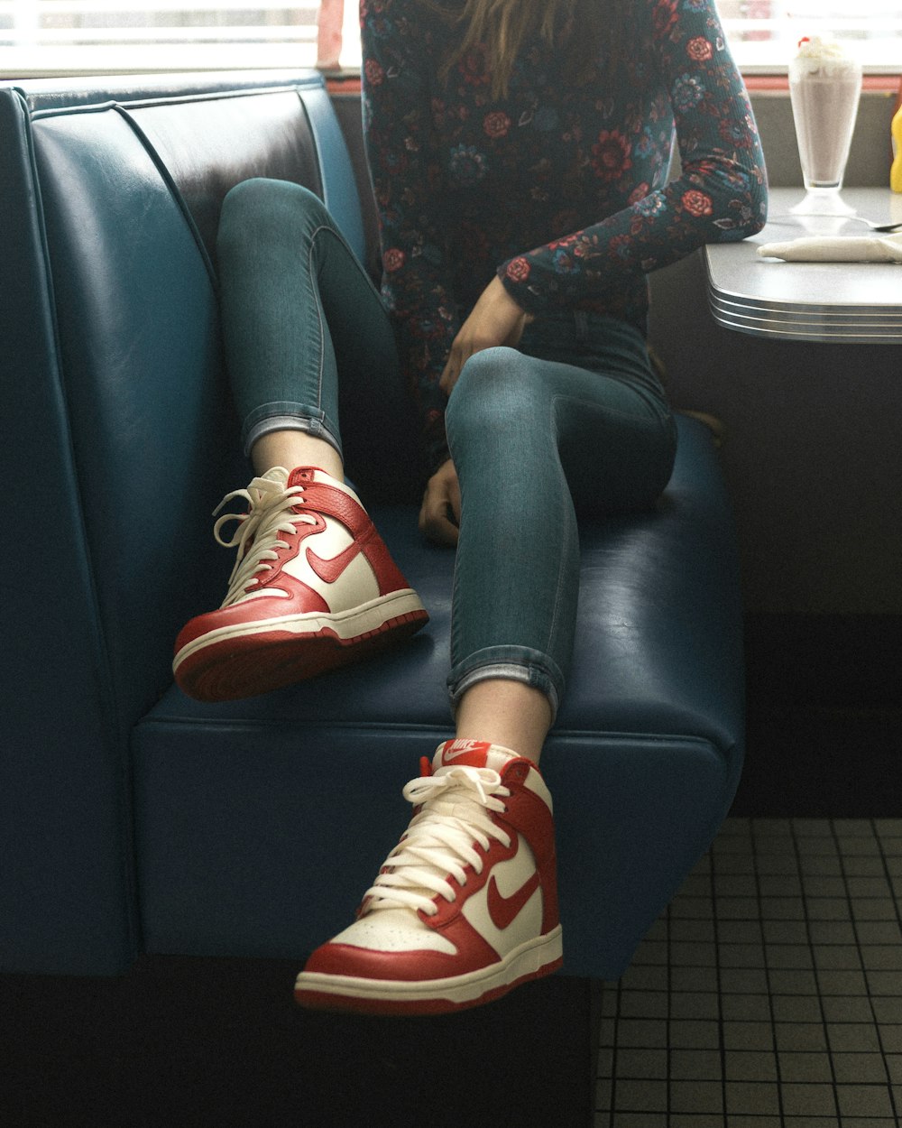 woman wearing red-and-white Nike mid-top sneakers while sitting on seat
