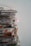 A tall stack of newspapers piled neatly against a plain background, with some publications appearing to show colorful images and text in a foreign language.