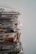 A tall stack of newspapers piled neatly against a plain background, with some publications appearing to show colorful images and text in a foreign language.