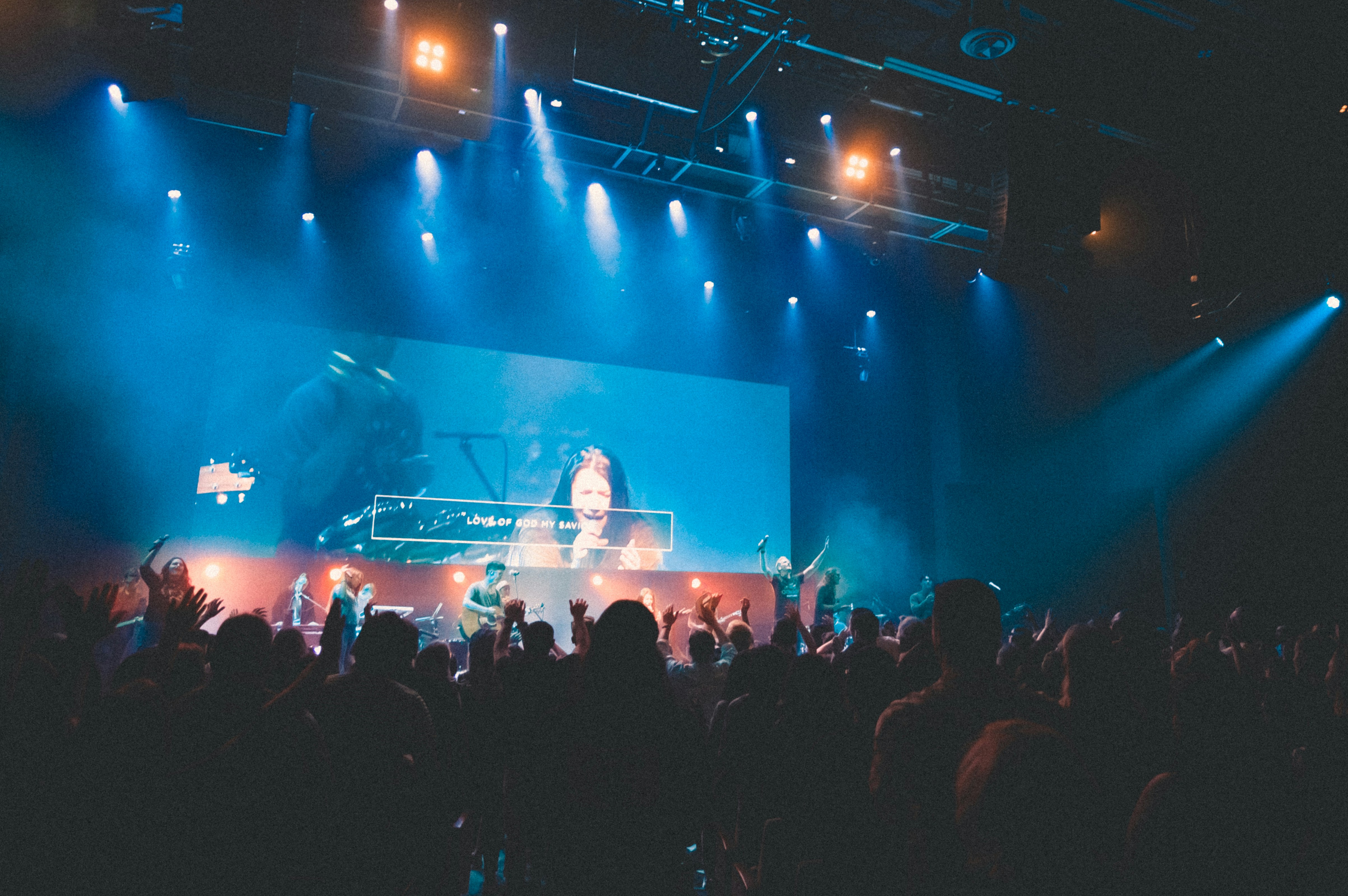Worshippers with raised hands in dimly lit sanctuary with stage lighting