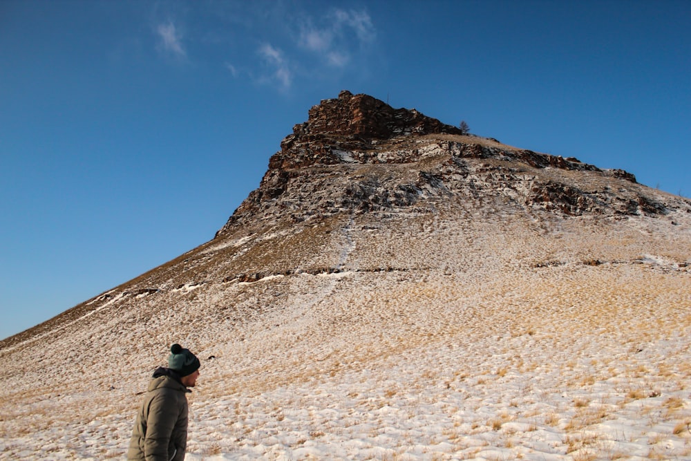 man wearing brown bubble jacket and gray knit cap beside brown mountain during daytime