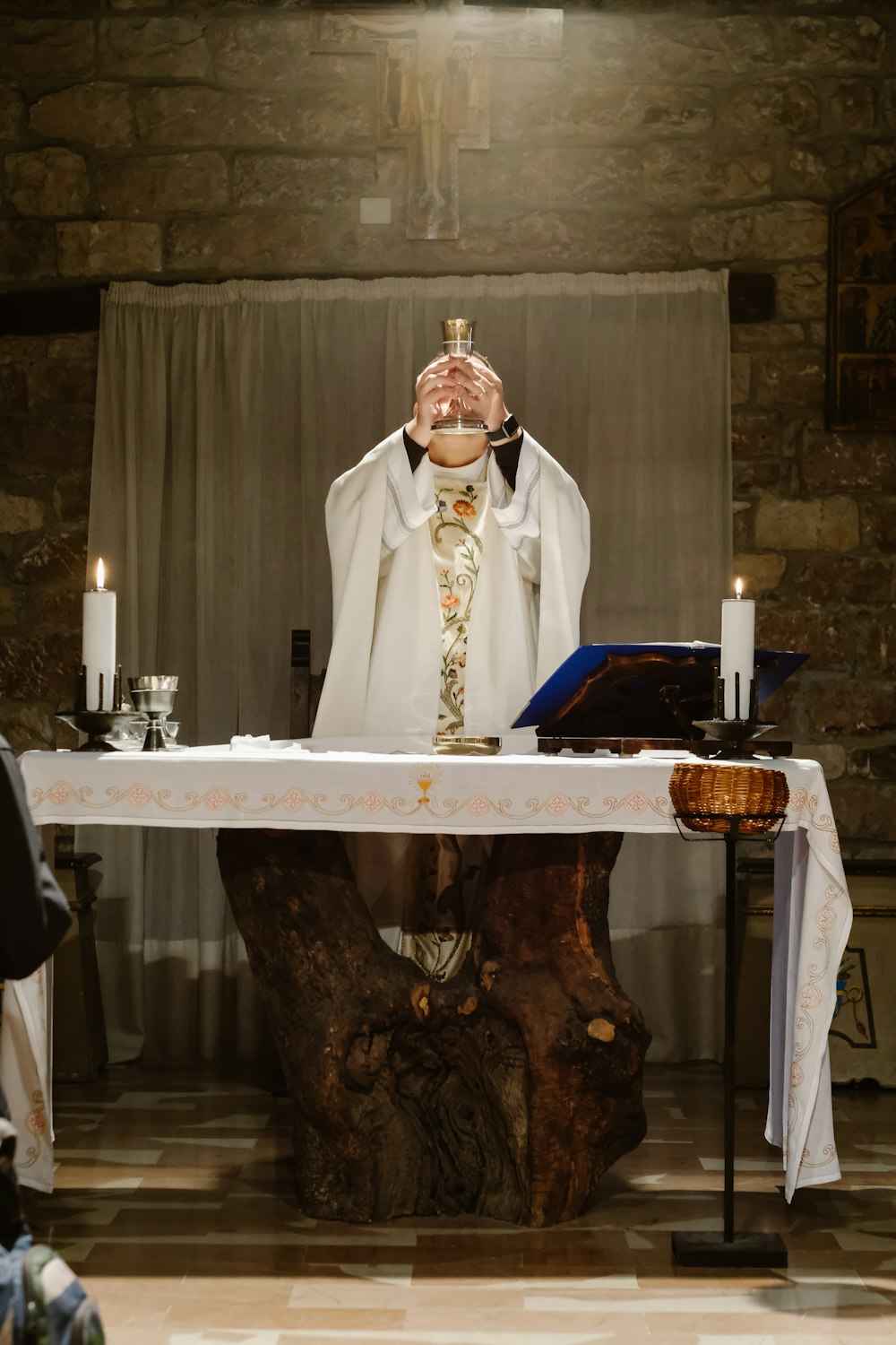 Priester hebt Becher an, während er neben dem Tisch steht