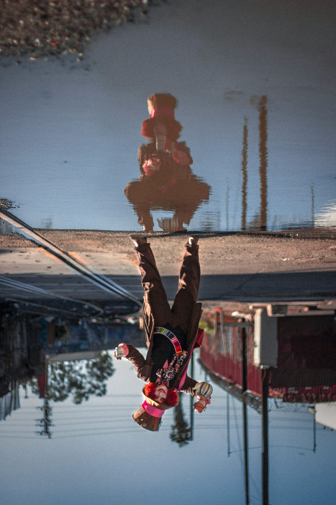 man posing as Mad Hatter besid water with self reflection during daytime