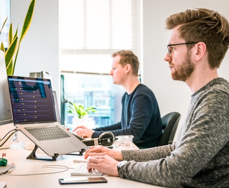 man sitting on chair wearing gray crew-neck long-sleeved shirt using Apple Magic Keyboard