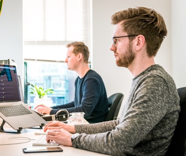 man sitting on chair wearing gray crew-neck long-sleeved shirt using Apple Magic Keyboard