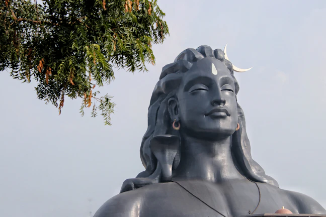 A serene statue of Lord Shiva with a glowing crescent moon atop his head amidst temple shadows.