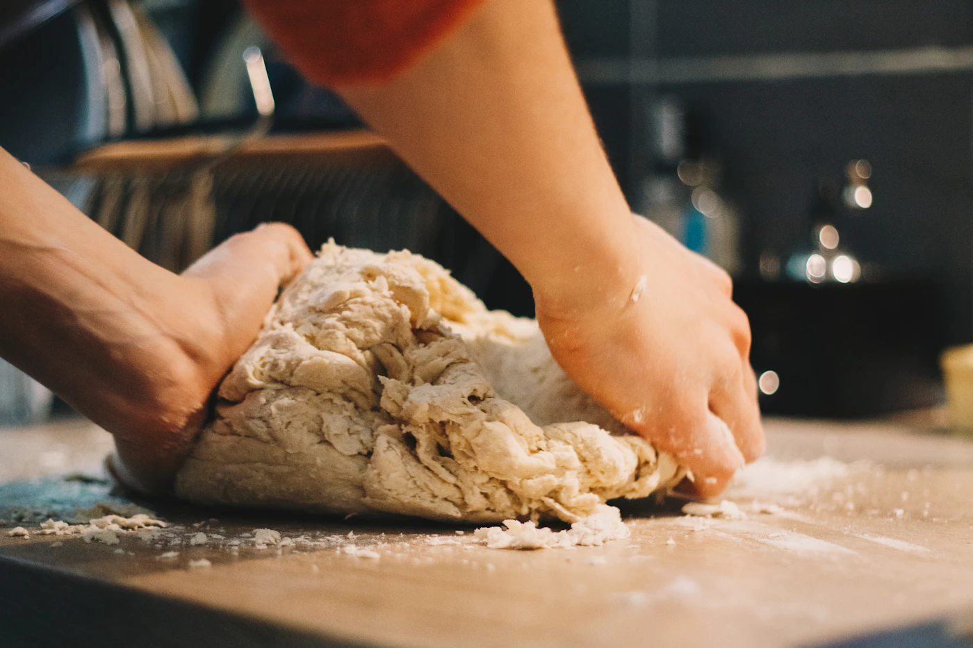 Hands working a ball of dough on a floured wooden board