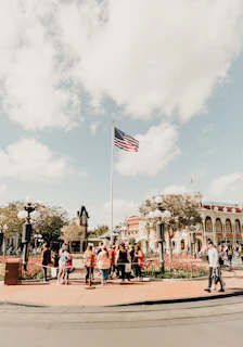 people standing and woman walking and standing by pole with USA flag