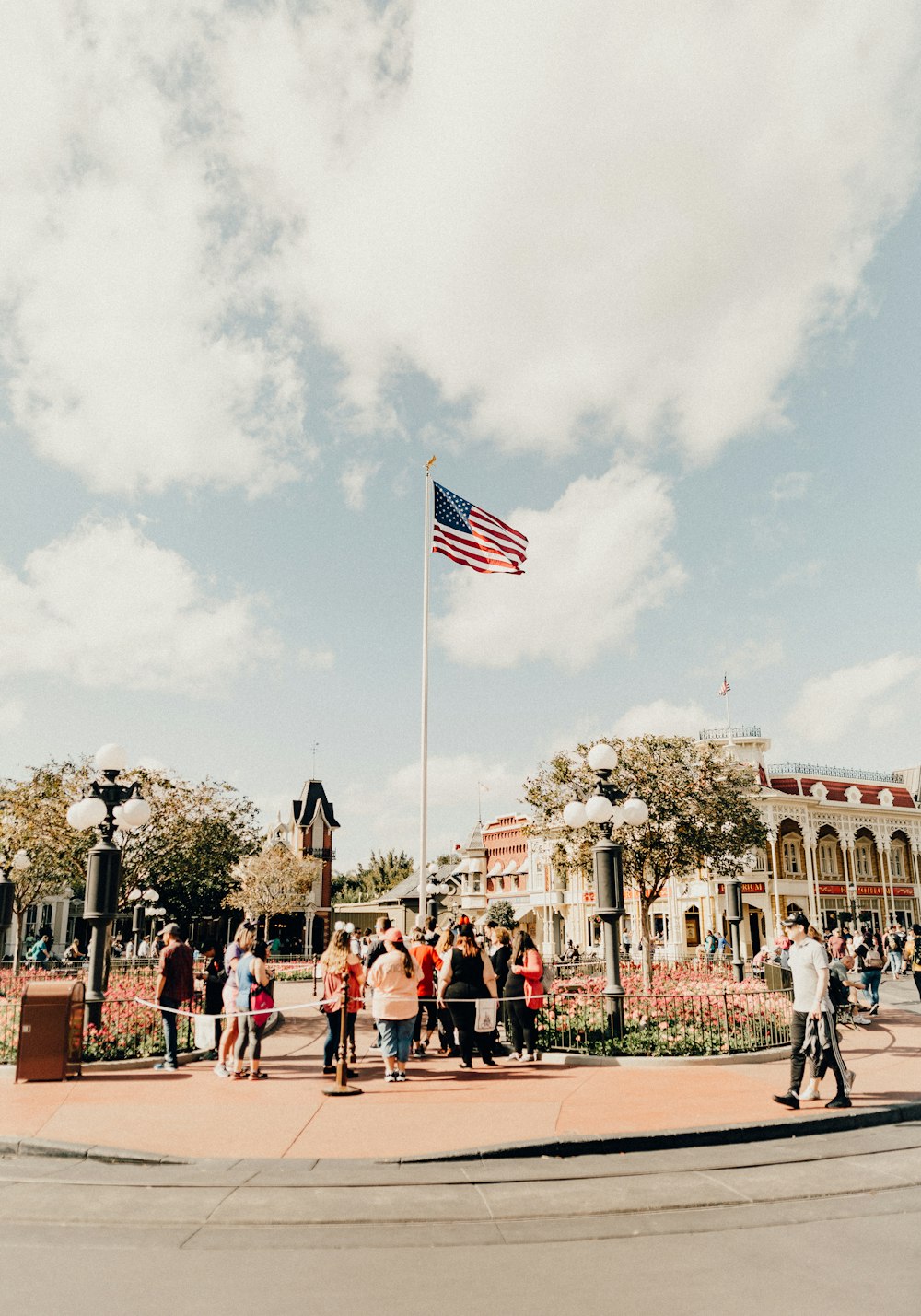 people standing and woman walking and standing by pole with USA flag