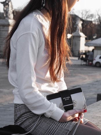 A candid moment of a woman adjusting her miharo bag strap while seated at a chic outdoor café.