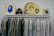 A clothing rack displaying a variety of white and colorful shirts, with a mix of plain and patterned designs. Positioned above the rack are several items including a colorful abstract artwork, a camouflage backpack, a yellow inflatable ring with text, and a book featuring a profile of a person.