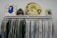 A clothing rack displaying a variety of white and colorful shirts, with a mix of plain and patterned designs. Positioned above the rack are several items including a colorful abstract artwork, a camouflage backpack, a yellow inflatable ring with text, and a book featuring a profile of a person.