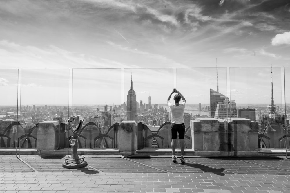 grayscale photography of man standing near tower viewer