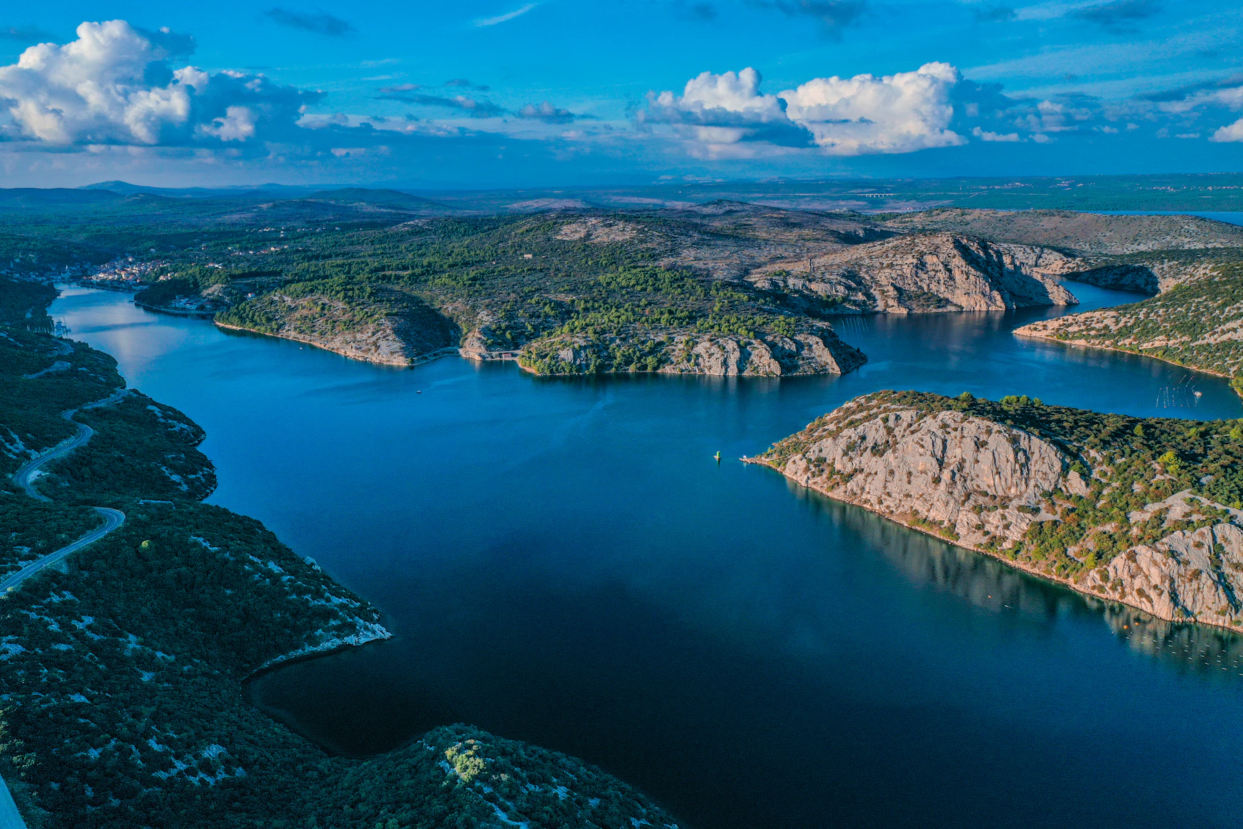 A low green island sits in clear blue water.