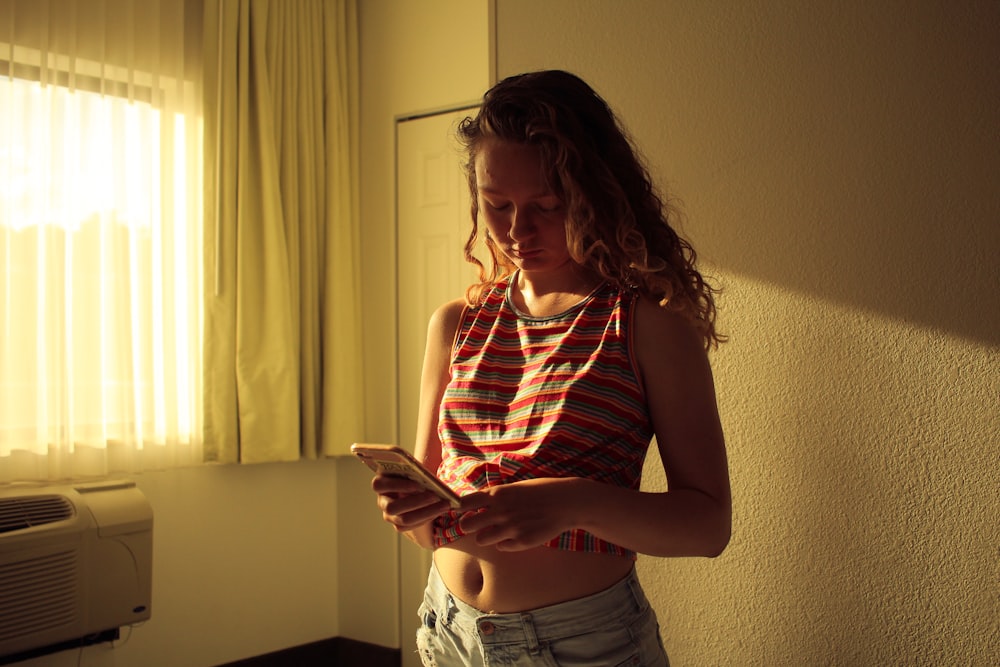 woman in red and gray tank top holding smartphone