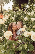 A tender moment between a mother and daughter surrounded by soft pastel blooms, both wearing delicate dresses.