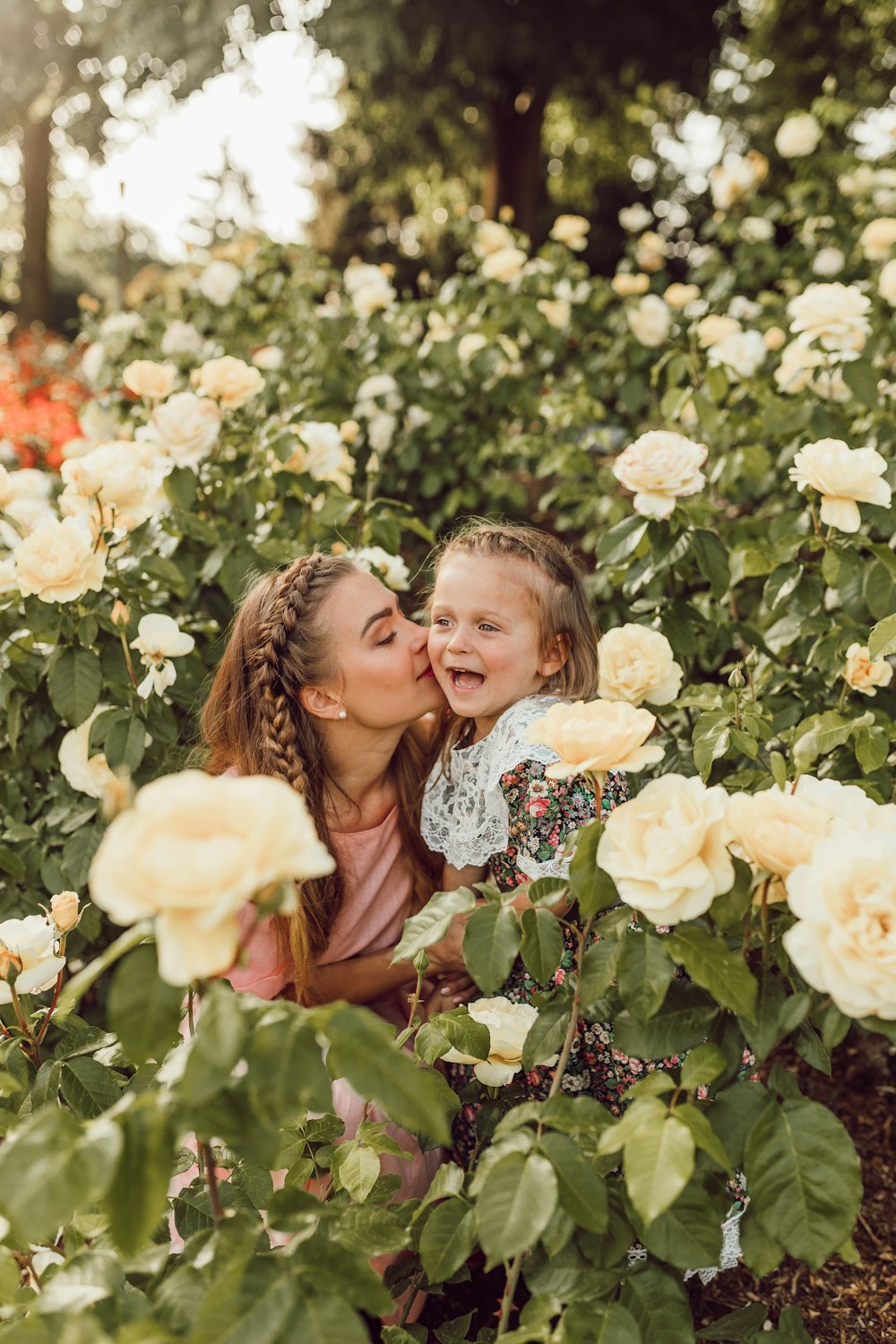 woman kissing girl's cheek between white roses garden