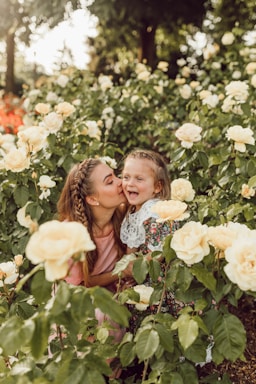 photography poses for family,how to photograph mother and daughter; woman kissing girl's cheek between white roses garden