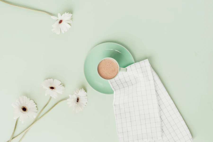 Pastel cup on a mint background with daisies