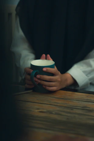 Smiling person holding a warm magic mug glowing with vibrant colors over a cozy amber-lit table.