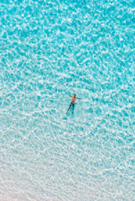 Close-up of a swimmer cutting through turquoise ocean waves under bright sunlight.