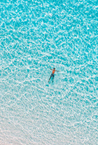 Close-up of a swimmer cutting through turquoise ocean waves under bright sunlight.