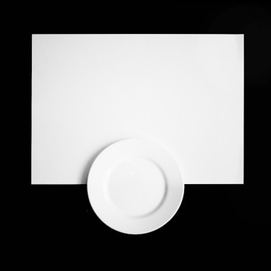 A white, empty circular plate is centered against a white rectangular background, with a contrasting black border surrounding the entire arrangement.