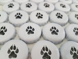 A collection of bottle caps arranged close together, each featuring a black paw print design on a white background.