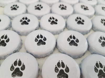 A collection of bottle caps arranged close together, each featuring a black paw print design on a white background.