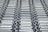 A repeating pattern featuring rows of metallic conveyor rollers arranged horizontally, creating a sense of industrial symmetry. The rollers have a shiny, reflective surface and are uniformly aligned, suggesting movement or transportation capabilities.
