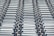 A repeating pattern featuring rows of metallic conveyor rollers arranged horizontally, creating a sense of industrial symmetry. The rollers have a shiny, reflective surface and are uniformly aligned, suggesting movement or transportation capabilities.